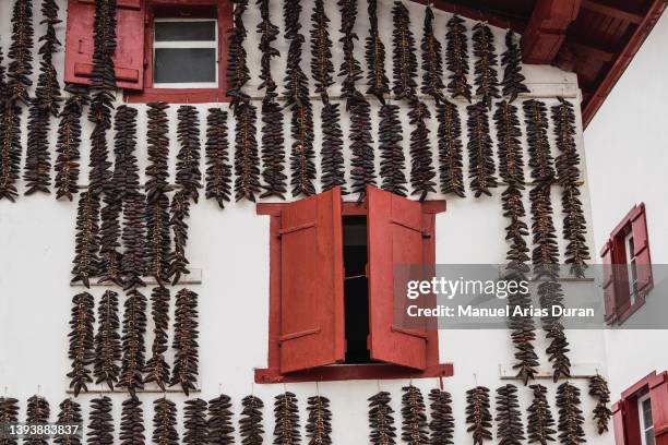 white facade with red wooden windows. on the facade there are hanging peppers drying. - baskenland stock-fotos und bilder