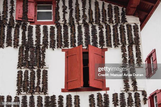 white facade with red wooden windows. on the facade there are hanging peppers drying. - espelette france photos et images de collection