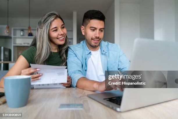 happy couple at home paying bills online - home finances imagens e fotografias de stock