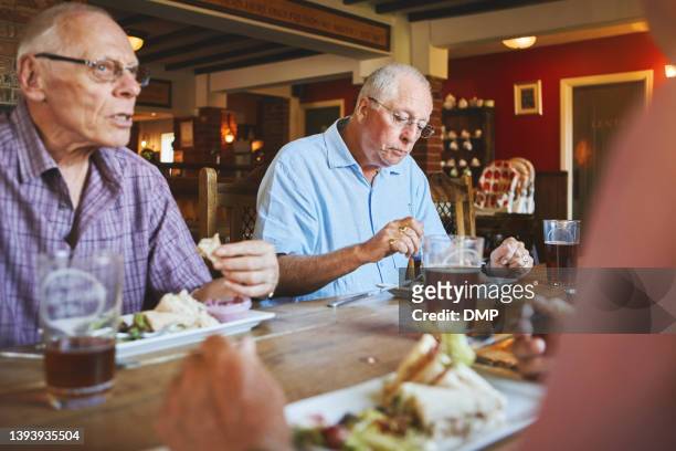 uomo anziano seduto con gli amici e godendo il pranzo in un bar. uomini anziani che si legano a pranzo in un pub, amici anziani - man eating at diner counter foto e immagini stock
