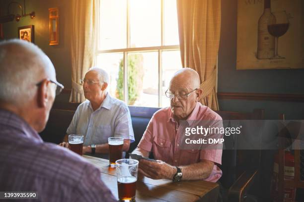 gruppe von älteren männern, die zusammen sitzen und kartenspiele in einer bar spielen, sich verbinden, ältere freunde, die eine partie bridge in einem pub genießen - thinking of you card stock-fotos und bilder