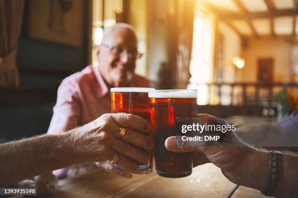 grupo de hombres mayores desconocidos sentados juntos y brindando con cerveza en un bar, uniéndose, amigos mayores disfrutando de una pinta de cerveza en un pub, vítores - cerveza-tipo-ale fotografías e imágenes de stock