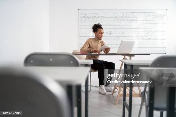 an african male teacher in an empty classroom teaches students online - closing laptop stock pictures, royalty-free photos & images