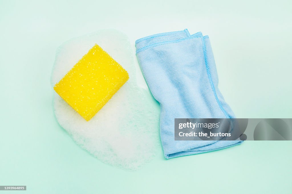 High angle view of a blue cleaning cloth and sponge on white foam on turquoise background