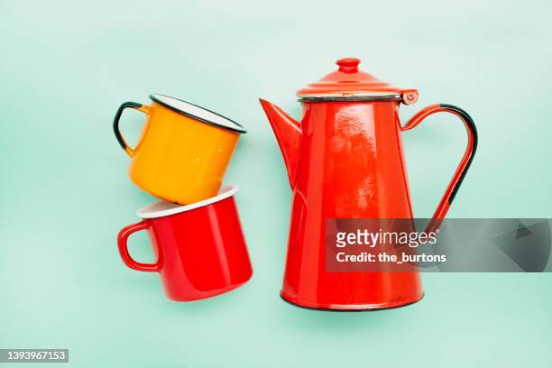 still life of two enamel cups and a red coffee pot on turquoise background - koffiepot stockfoto's en -beelden
