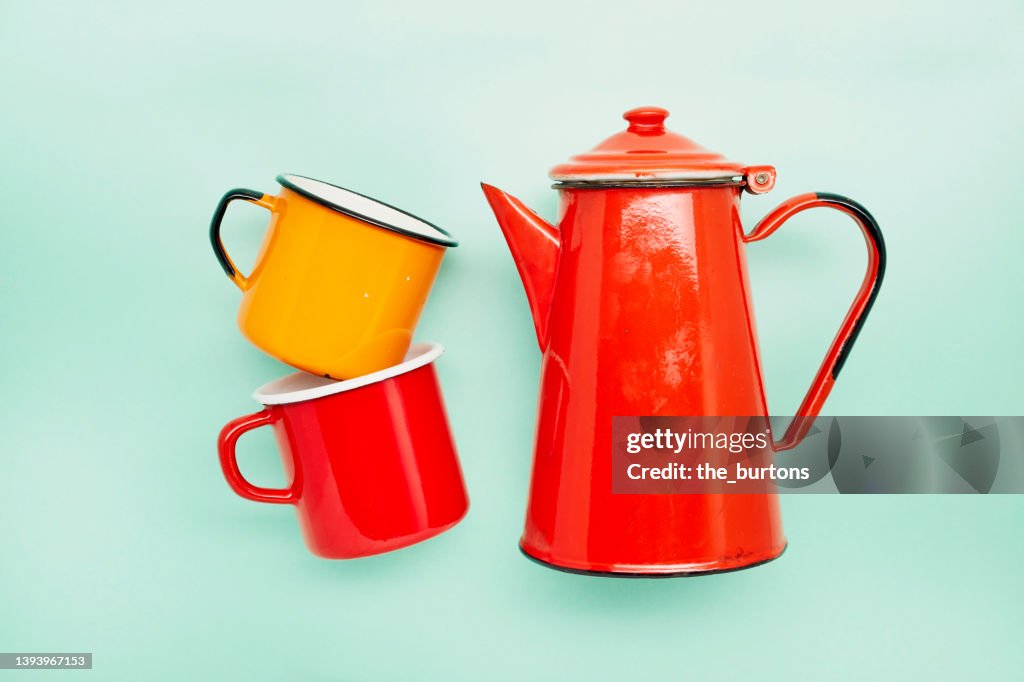 Still life of two enamel cups and a red coffee pot on turquoise background