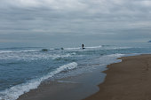 Inclement weather is no impediment to water sports. Man surfs small waves with paddle surf on the beach of the Mediterranean Sea on a cloudy day.
