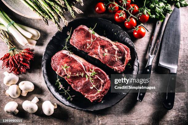 two raw beef steaks on a black plate, in the kitchen on the counter - top of view. - rood vlees stockfoto's en -beelden