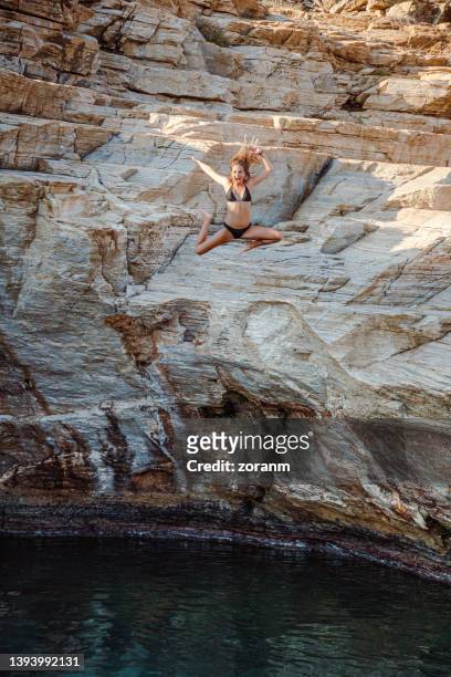 giovane donna in bikini che si tuffa nell'acqua di mare dalla scogliera in posa sciocca - cliff diving foto e immagini stock