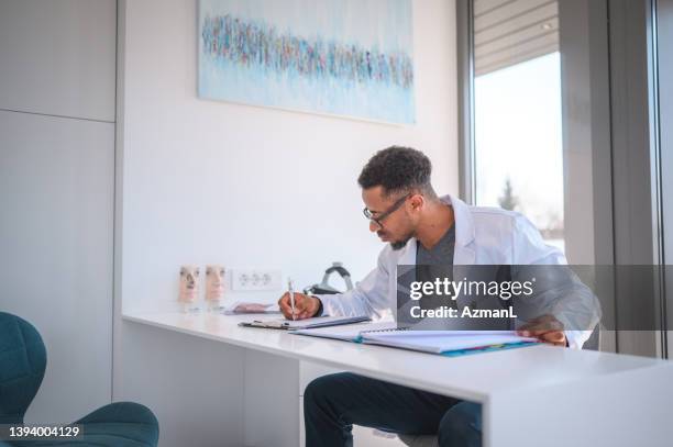 african american doctor writing a medical chart - gp practice stock pictures, royalty-free photos & images