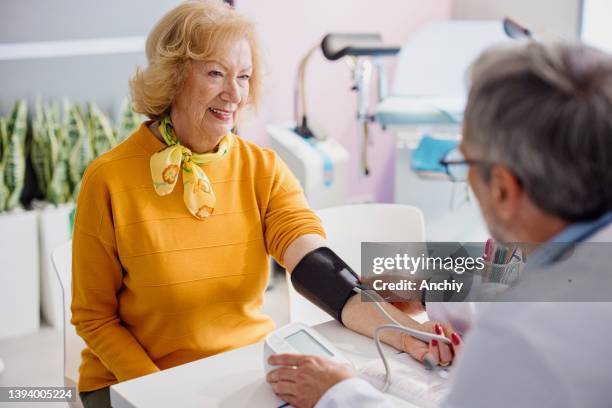 doctor checking female patients blood pressure in clinic - high blood pressure stock pictures, royalty-free photos & images