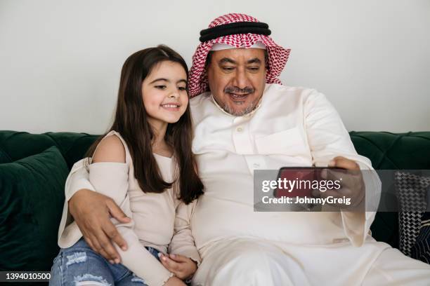 saudischer mann und enkelin nutzen smartphone zusammen - two young arabic children only indoor portrait stock-fotos und bilder