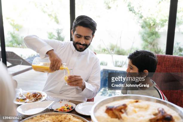 middle eastern father pouring juice for son at dining table - young muslim man stockfoto's en -beelden