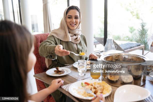 lächelnde saudische frau in den späten 20er jahren, die ihrer tochter essen serviert - saudi youth stock-fotos und bilder