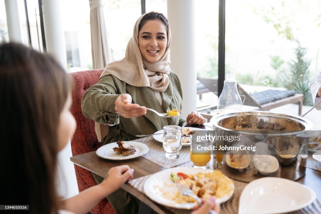 Smiling Saudi woman in late 20s serving food to daughter