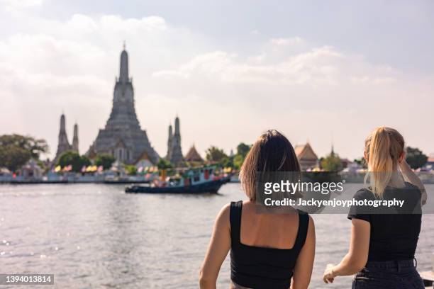 two young caucasian women looking and shooting photos with wat arun temple enjoy the vacation in bangkok,thailand. - menam stockfoto's en -beelden