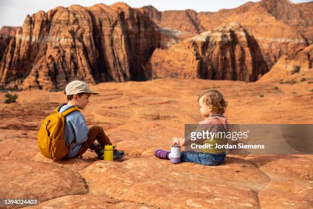 two young kids having a water break while hiking in the desert. - utah hiking stock pictures, royalty-free photos & images