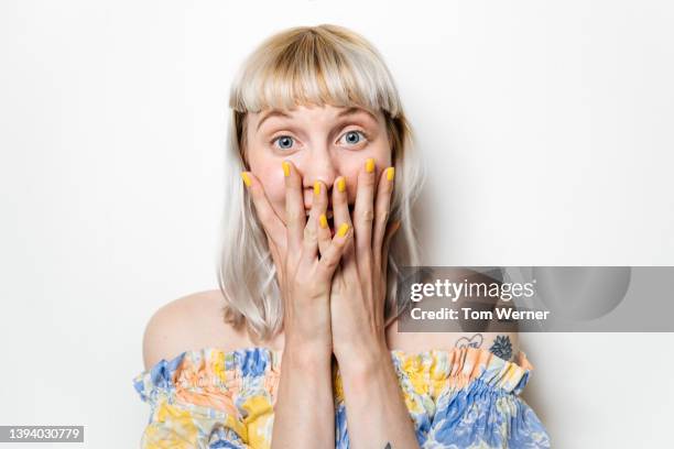 portrait of excited blond woman with hands covering mouth - überrascht stock-fotos und bilder