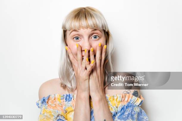 portrait of excited blond woman with hands covering mouth - ongeloof stockfoto's en -beelden