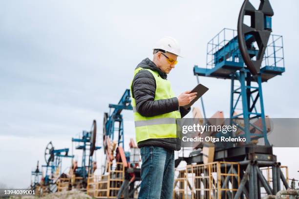 professional worker in a protective helmet, glasses and green vest writes data into a tablet at oil enterprise - working oil pumps stock pictures, royalty-free photos & images