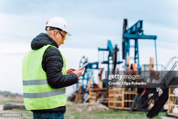 drill worker calculating data on tablet, oil refinery tasks near pump jack, processing facility. oil industry - my tablet tool stock-fotos und bilder