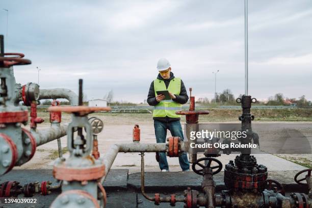 stationary or technical engineer at work, checking valve pipes, calculating and analyzing charge of oil and gas in digital tablet - industria petrolchimica foto e immagini stock