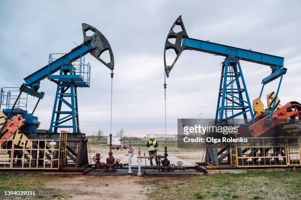 oil pumps, nodding donkey or pump jack and rig against blue cloudy sky. engineer in protective uniform working in between - russia photos et images de collection