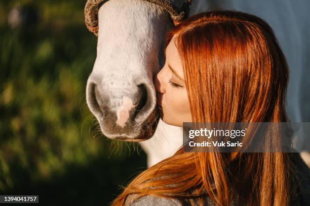 a red-haired woman kissing a horse in a snout - horse eye stockfoto's en -beelden