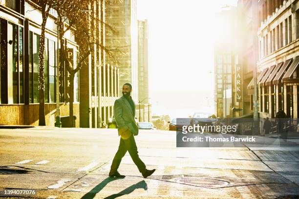 wide shot of smiling businessman walking across downtown street - 背景人物 個照片及圖片檔