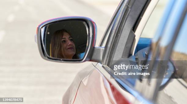 rear view of the car mirror of mature blond woman driving on the road trip - side view mirror foto e immagini stock