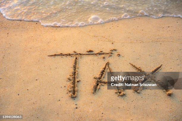 tax text written on sand beach with waves - federal budget stockfoto's en -beelden