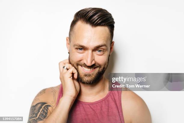 portrait of man smirking while scratching beard - tattoo shoulder stock-fotos und bilder