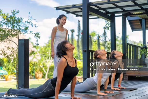 full length of female instructor assisting group of senior woman in practicing yoga. elderly lady is exercising yoga. they are in sportswear at health club. - yoga instructor stock pictures, royalty-free photos & images