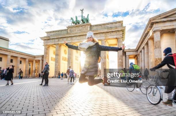 young woman jumping in front of brandeburg gate in berlin - brandenburger tor stock pictures, royalty-free photos & images