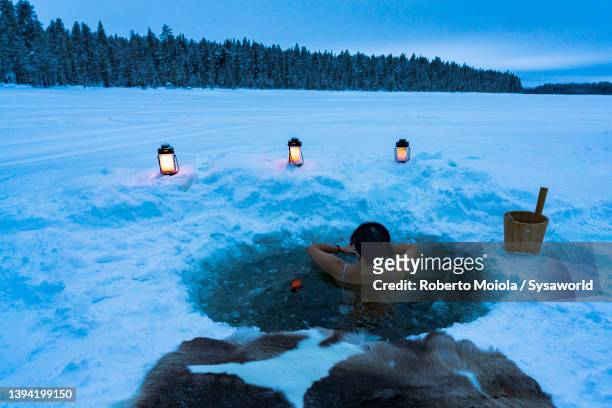 woman enjoying cold baths in a ice hole, lapland - cryotherapy stockfoto's en -beelden