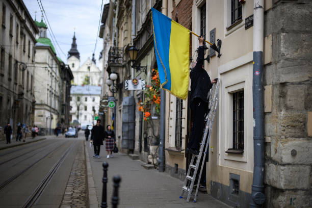 Man hangs a Ukrainian flag outside a business on April 28, 2022 in Lviv, Ukraine. Lviv has served as a stopover and shelter for the millions of...