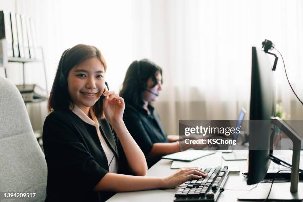 porträt eines jungen call-center-agenten, der ein mobiltelefon benutzt, während er in einem büro arbeitet - halb mann halb frau stock-fotos und bilder