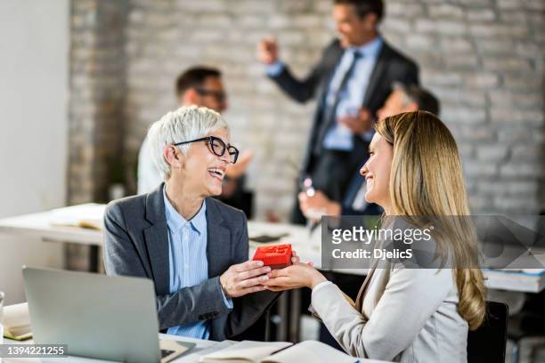 happy senior businesswoman receiving a gift from her female colleague in the office. - happy office workers stockfoto's en -beelden