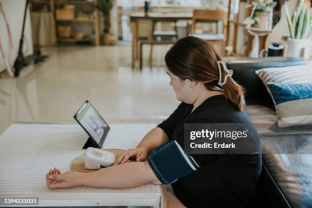 telemedicine, asian plus size woman checking her blood  and heart rate pressure by herself at home. - fat asian woman stock pictures, royalty-free photos & images