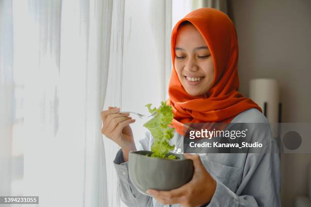 muslimische frau, die zu hause grünen salat isst. - malay hijab stock-fotos und bilder