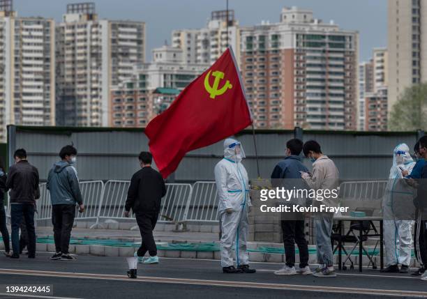 Communist Party of China flag is seen next to a health worker wearing protective clothing as office workers line up for nucleic acid tests to detect...