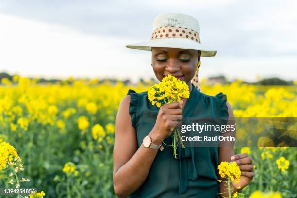 woman portrait holding and smelling yellow flowers bouquet on colorful countryside field - green hat fotografías e imágenes de stock