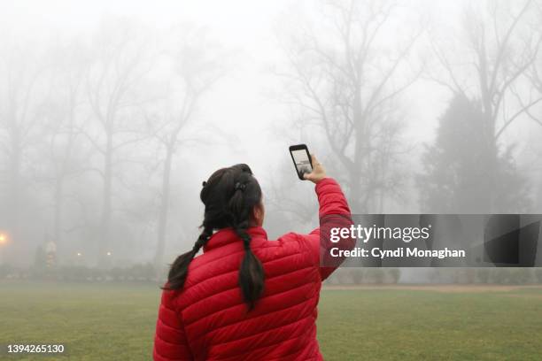 woman photographing the mist and fog on a winter day. - femme de dos smartphone photos et images de collection