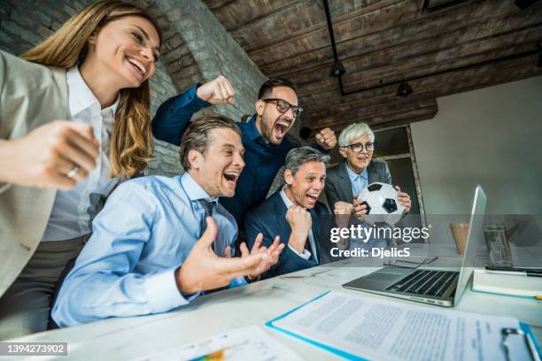 cheerful business people cheering while watching their sports team on computer in the office. - office excitement stock pictures, royalty-free photos & images
