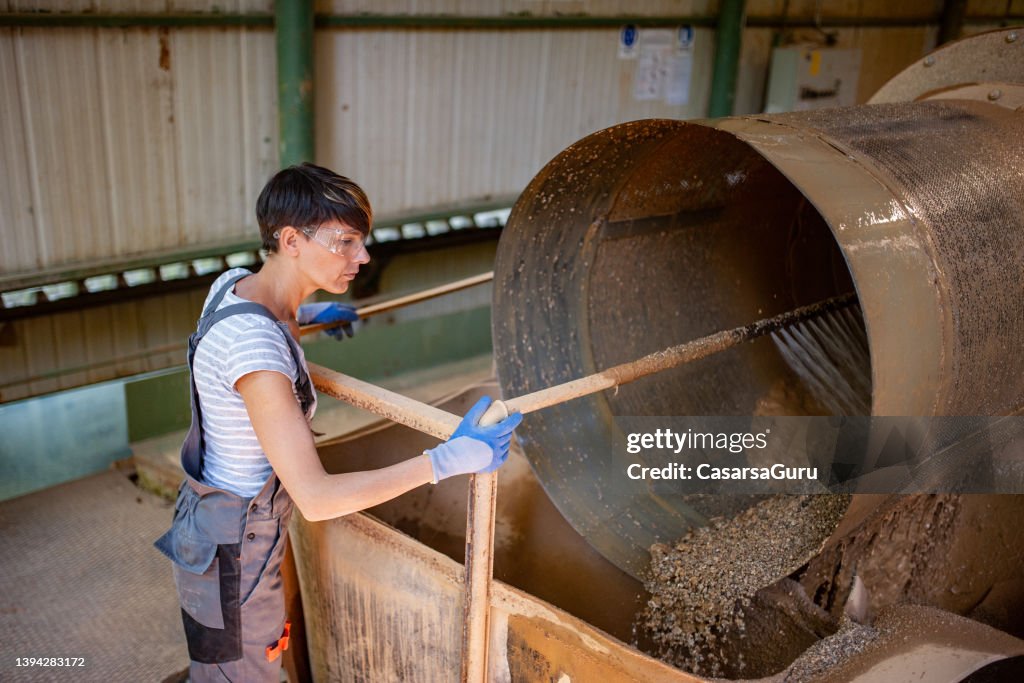 Blue-collar woman standing next to a rode mill in the Quartz ore Processing plant