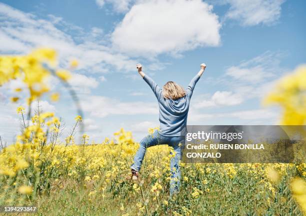 enthusiastic young woman jumping in oilseed rape field on sky background - les bras écartés photos et images de collection