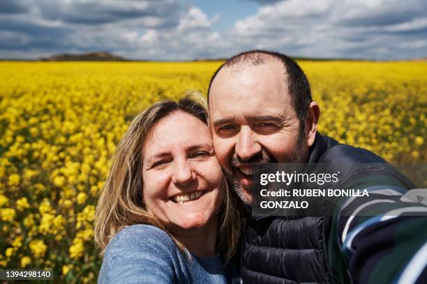 happy caucasian heterosexual couple having fun taking selfie in oilseed rape meadow. travelling concept - older couple travelling photos et images de collection