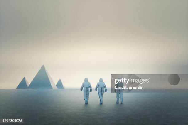 astronauts walking towards mysterious pyramids - astronaut stock pictures, royalty-free photos & images