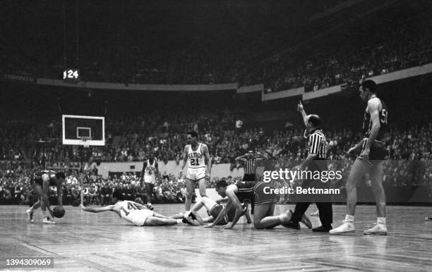 Celtics' Bob Cousy comes slithering out of a pile up on his stomach to try to loose the ball that Saint Louis Hawks', Slater Martin has just scooped...