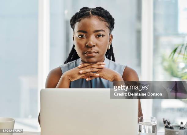 young african businesswoman looking serious while working on a laptop in an office alone - authentic real stockfoto's en -beelden